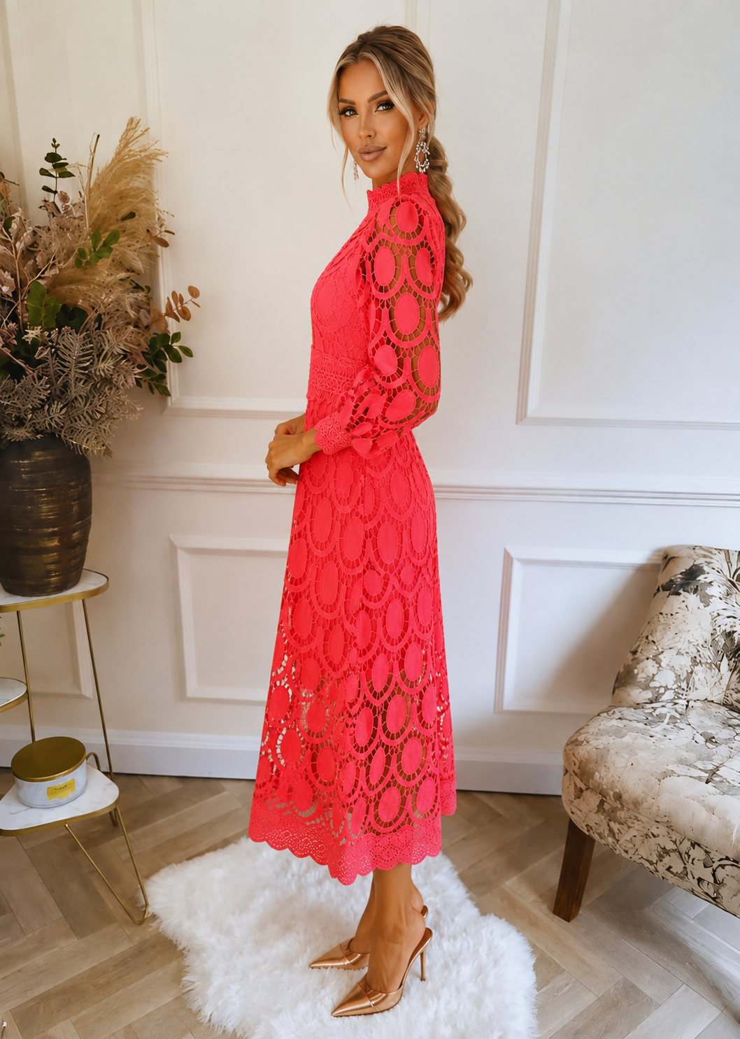 Woman in a pink lace dress standing in a stylish room with decor elements.