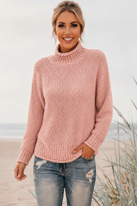 Woman wearing a pink Skye knitted sweater and jeans on a beach.