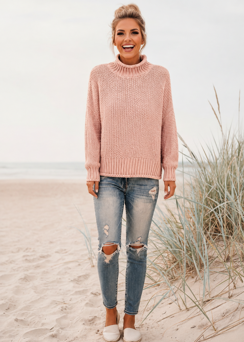 Woman wearing a Villa Vibes pink Skye sweater and ripped jeans on a beach