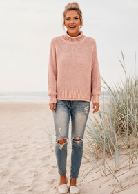Woman wearing a Villa Vibes pink Skye sweater and ripped jeans on a beach