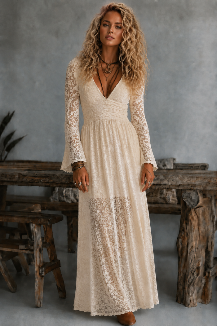 Woman wearing a long, cream Tessa lace dress from Villa Vibes in a rustic setting.