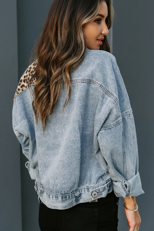 Woman wearing a Villa Vibes light blue denim trucker jacket with a leopard print patch on a gray background