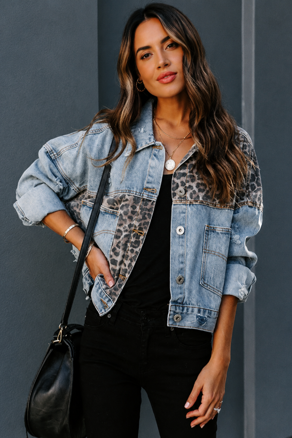 Woman wearing a Villa Vibes Kia denim trucker jacket with leopard print accents against a gray background