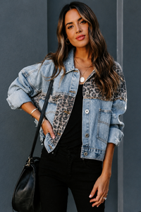 Woman wearing a Villa Vibes Kia denim trucker jacket with leopard print accents against a gray background