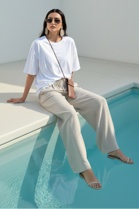 Woman sitting by a pool wearing a white t-shirt and Villa VIbes Tianna beige pants.