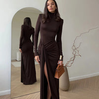 Woman in a Villa VIbes Allegra brown dress standing in front of a mirror, holding a brown handbag.