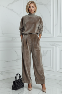 Woman wearing a Villa Vibes Aster brown velvet outfit with a black handbag against a white paneled wall.