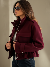 A woman wearing a Villa Vibes Blaise burgundy cropped jacket with silver-tone hardware, styled with dark blue jeans and sunglasses against a neutral beige background.
