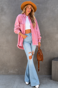 Woman wearing a Brydie pink jacket, white top, and blue jeans against a gray wall.