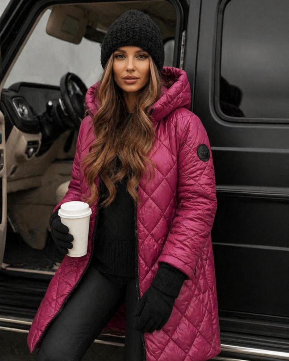 Woman in a Villa Vibes Camron Rosequilted coat and black beanie holding a coffee cup, standing next to a vehicle.