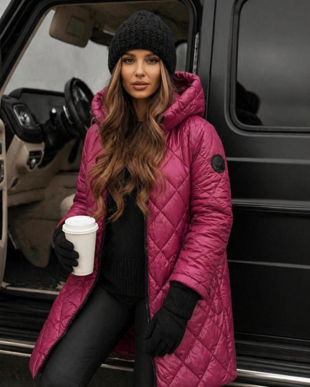 Woman in a Villa Vibes Camron Rosequilted coat and black beanie holding a coffee cup, standing next to a vehicle.