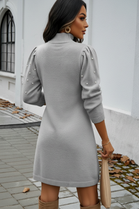 Woman wearing a Villa VIbes Chelsea gray sweater dress with pearl details in an urban setting.