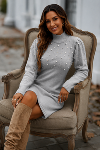 Woman in a Villa Vibes CHelsea gray sweater dress with pearl embellishments sitting on a chair outdoors.