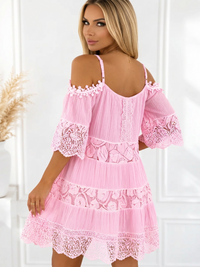 A woman wearing a Villa Vibes Fallon light pink cold-shoulder mini dress with lace trim and tiered ruffles, shown from the back in a bright indoor setting.