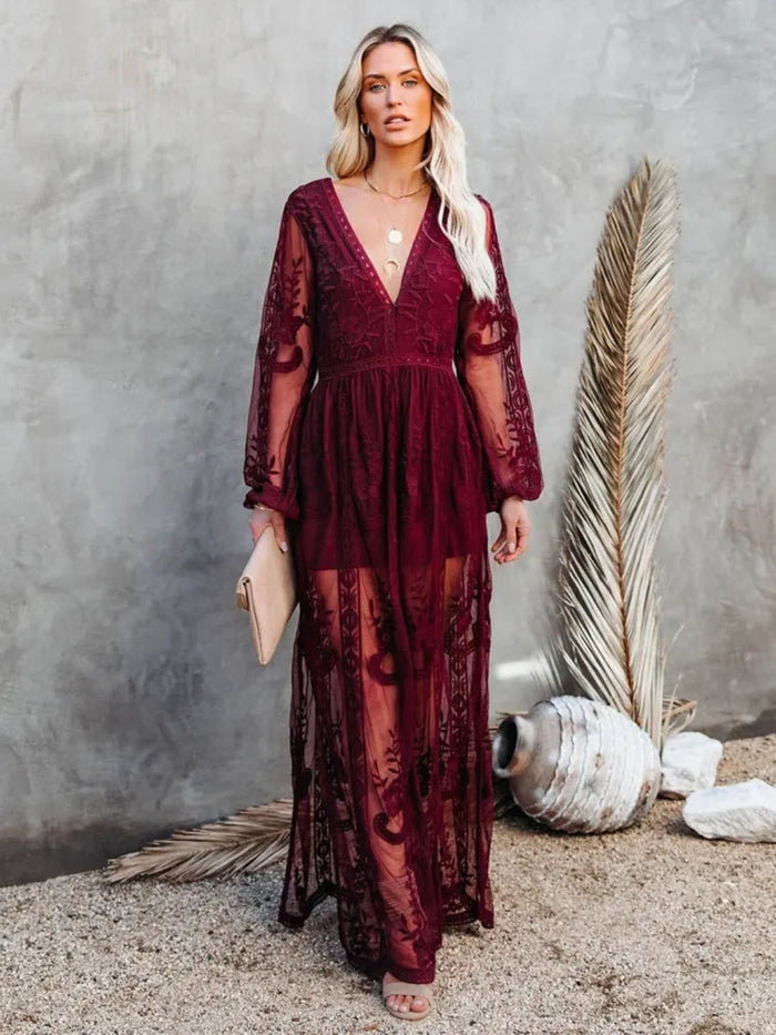 Woman wearing a Villa Vibes Janis burgundy lace dress against a gray wall with decorative elements.