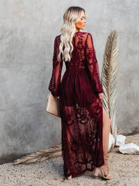 Woman in a Villa Vibes Janis burgundy lace dress standing against a textured wall with a dried palm leaf.