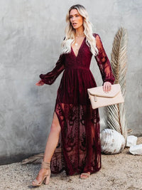 Woman in a Villa Vibes Janis burgundy lace dress holding a beige clutch against a gray wall.