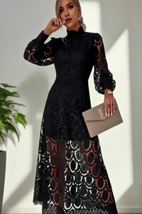 Woman wearing a Villa Vibes Jasmine black lace dress holding a beige clutch against a white wall.