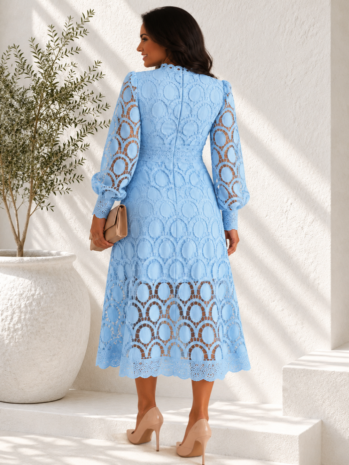 A woman wearing a Villa Vibes Jasmine light blue lace midi dress with long sleeves and an allover circular lace pattern, shown from the back in a bright, sunlit interior setting.