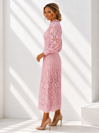 A woman modeling a Villa Vibes Jasmine light pink long-sleeve lace midi dress with a high mock neck and scalloped circular lace pattern, paired with beige high heels, standing in a bright white room with diagonal sunlight shadows.