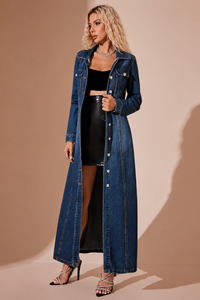 Woman wearing a Villa Vibes Jordie long denim jacket over a black outfit on a beige background