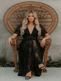 Woman in Villa Vibes Lotus black dress sitting on a decorative chair with a neutral background