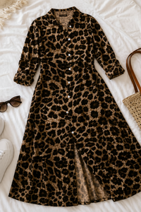 A Villa VibesMika leopard-print long-sleeve button-front dress laid flat on white bedding, styled with sunglasses, white sneakers, a woven tote bag, and a small pouch.