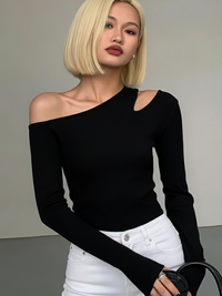 Woman wearing a Villa Vibes Nikki black one-shoulder top and white pants against a neutral background