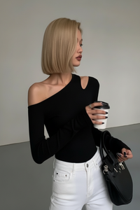 Woman in a Villa Vibes Nikki black off-shoulder top and white pants holding a coffee cup and black handbag.