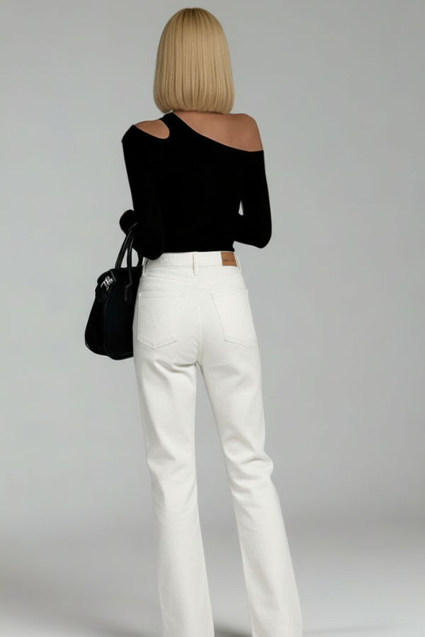 Person wearing a Villa Vibes Nikki black off-shoulder top and white pants, holding a black handbag on a plain background