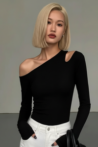 Woman wearing a Villa Vibes Nikki black one-shoulder top and white pants against a neutral background