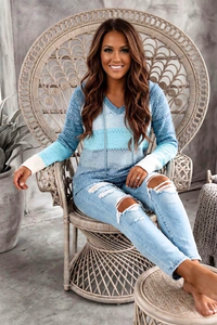 Woman sitting on a decorative chair wearing a Villa Vibes Pippa blue sweater and ripped jeans.