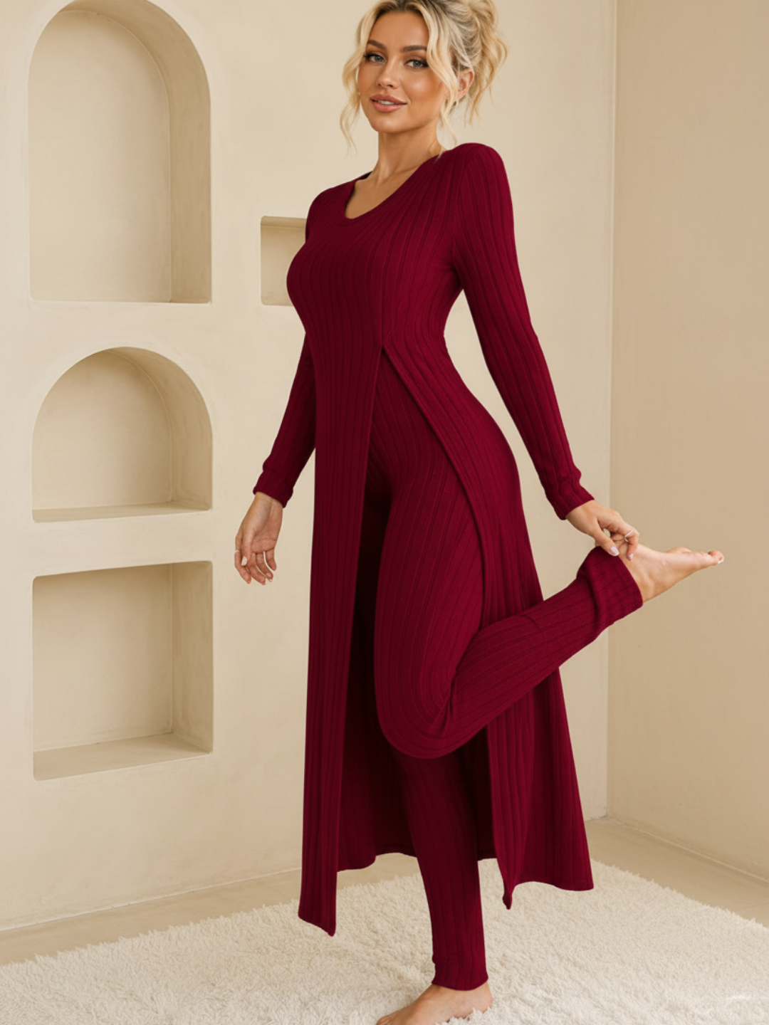 A woman modeling a Villa Vibes Shivani long-sleeve ribbed knit dress in deep burgundy, standing in a warm beige room with built-in arched shelves.