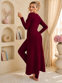 A woman wearing a Villa Vibes Shivani long-sleeve, ribbed knit 2pc set in deep burgundy, standing in a warm, beige-toned room with built-in shelves, curtains, and a rug.