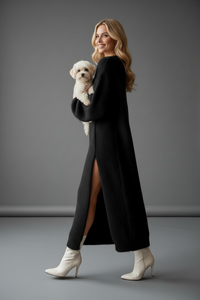Woman in a Villa Vibes Taylor long black coat holding a small white dog on a gray background