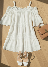 Villa Vibes Fallon White off-shoulder dress with ruffled details, white sandals, and a brown handbag on a wooden floor.