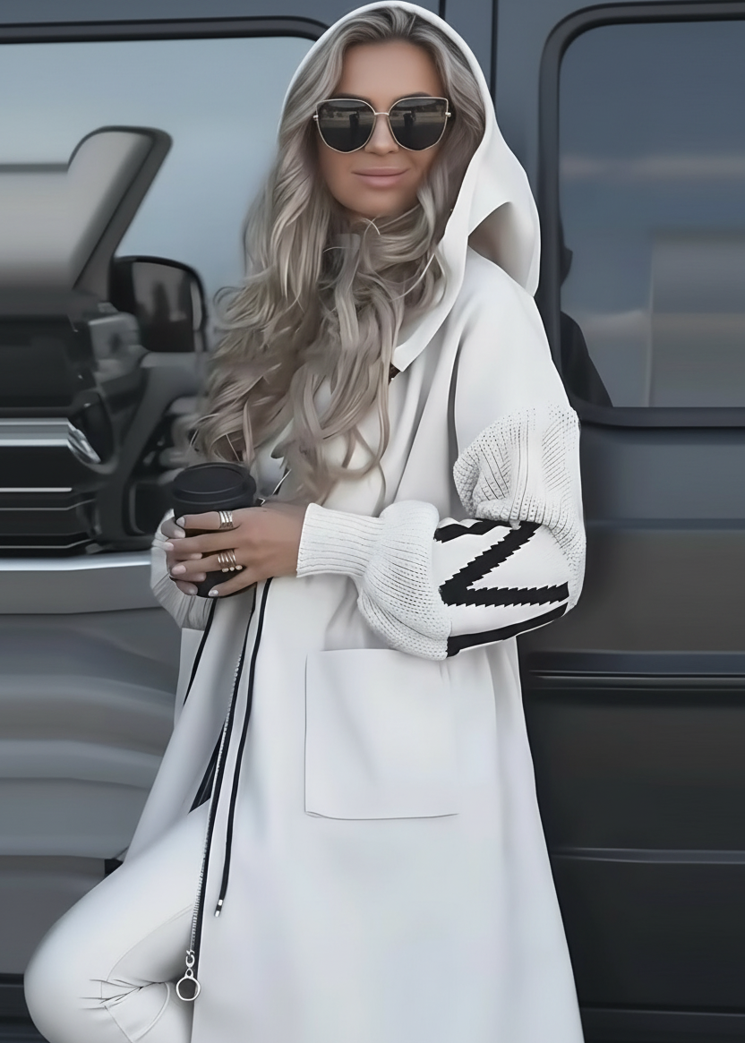 Woman in Kelly white coat with black and white patterned sleeves standing next to a vehicle.