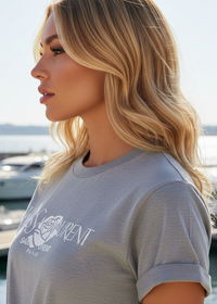 Woman wearing a gray t-shirt with a brand logo, standing outdoors.