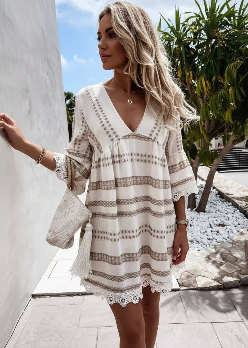 Woman wearing a white dress with brown patterns in an outdoor setting.