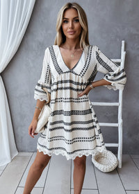 Woman wearing a white dress with black patterns, holding a white bag indoors.