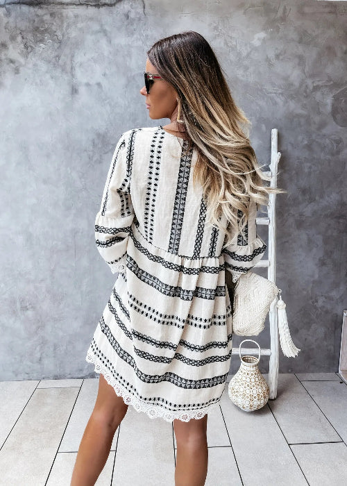Woman wearing a black and white patterned dress standing against a gray wall.