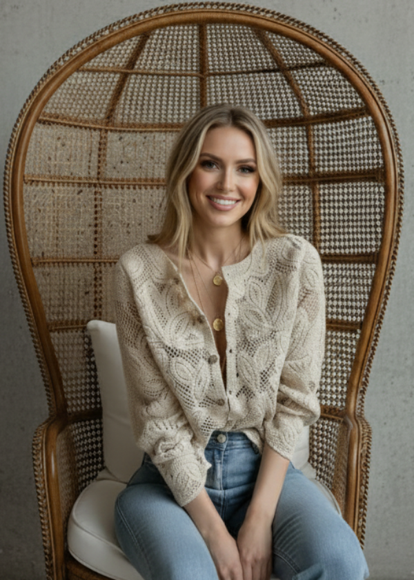 Woman sitting on a wicker chair wearing Roxy beige cardigan and blue jeans against a textured wall.