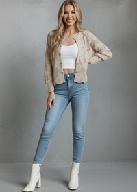Woman wearing Roxy beige cardigan, white top, blue jeans, and white boots on a gray background
