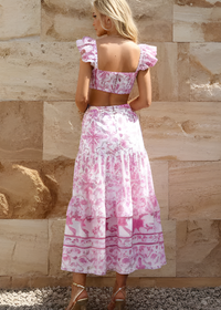Woman wearing Melania pink floral dress back view against a stone wall.