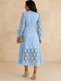 A woman shown from the back wearing a Villa Vibes Jasmine light blue lace midi dress with long sleeves and a fitted waist, standing against a beige stone wall and floor.